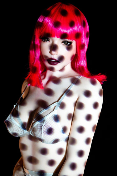 Person with polka dot hair and body paint against a black background
