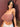 Woman wearing a sheer mauve top and white skirt against a brown background