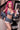 Person with pink hair wearing a denim outfit and holding headphones in an indoor setting.
