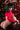 Person with green hair wearing a red outfit in front of a decorated Christmas tree and colorful wall.