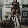Woman in a black dress sitting on a stool in a room with decor elements.