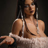 A realistic sex doll with long brown hair, wearing a pink fluffy outfit and white necklace. She has a lifelike appearance with detailed facial features and is accessorized with a belt and earrings.
